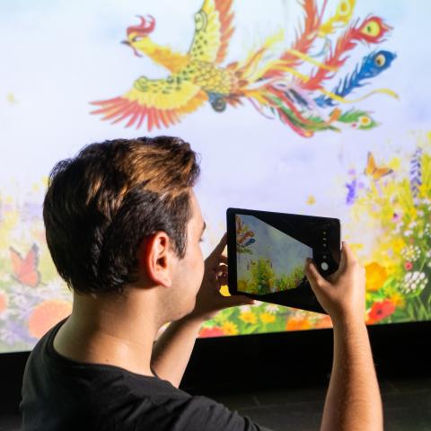 photo of student holding ipad with colorful background projected on a screen
