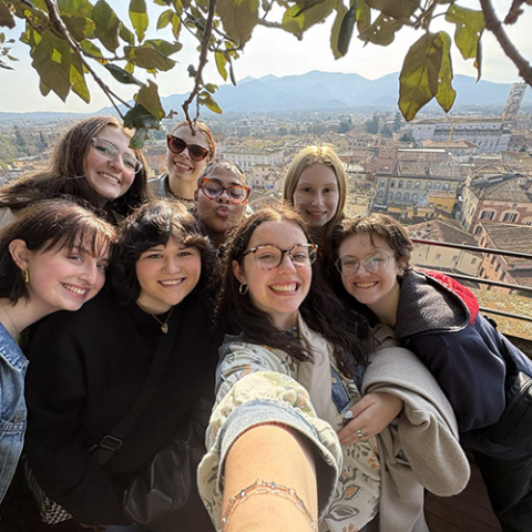 Image of 8 students taking a selfie together with an overlook of Florence, Italy in the background.