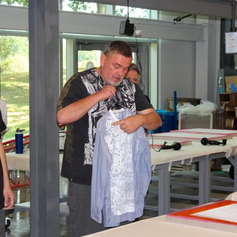 Man standing in the DI Hub Reactor Makerspace holding a blue shirt that has been screen printed. 