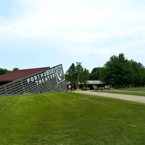 Porthouse Theatre Box Office building on a grass covered hill with a blue sky above. 