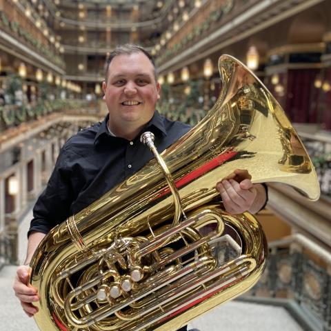 Man holding a tuba standing inside a building