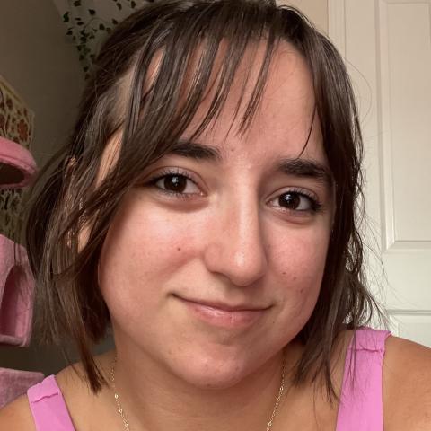 Meg in a bright pink tank top taking a selfie with a small smile with her short brown hair and bangs framing her face. 