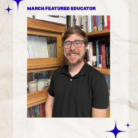 Man with brown shirt and glasses with books in background