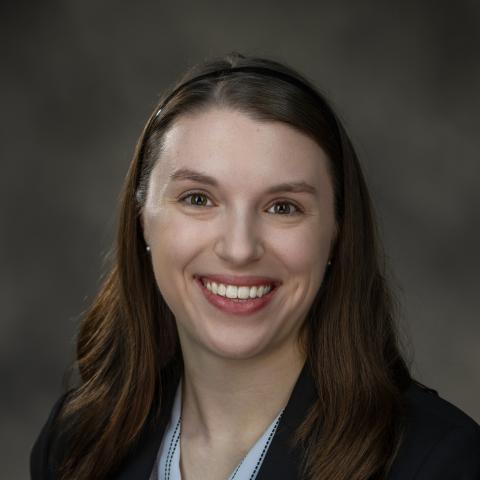 Headshot of Rachel wearing a blue shirt with black jacket overtop of it. She has long brown hair and is smiling.