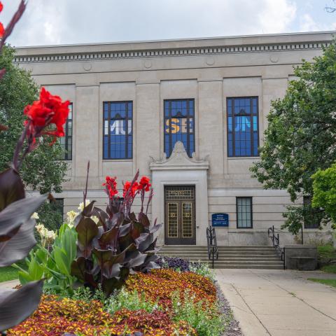 Light beige building with "Museum" showcased on its front and red flowers framing the image