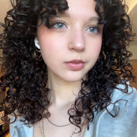 Caley looking at the camera in a selfie with her dark curly hair framing her face.