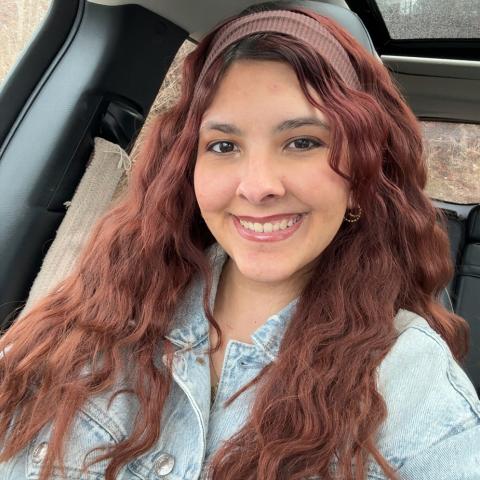 Elle smiling brightly at the camera with her long red hair and denim long-sleeve shirt. 