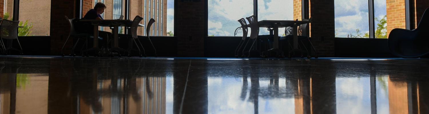 A student working at a laptop, the large windows in the Student Center behind him.