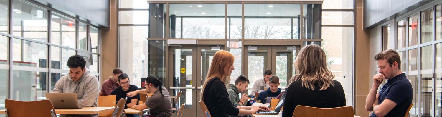 students sitting in the AEB atrium under a sign with the text "Dare Mighty Things"