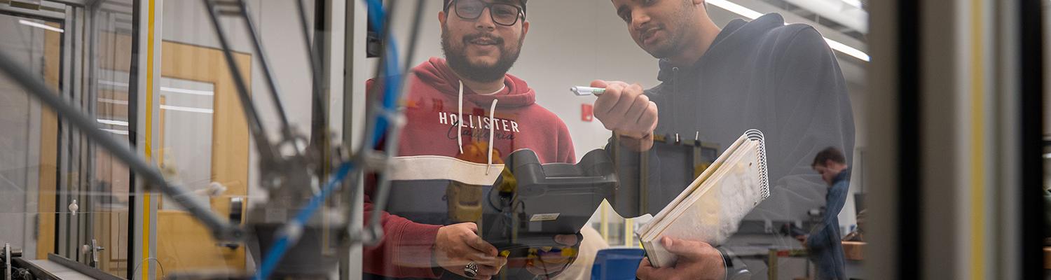 Two students examine the workflow between two autonomous manufacturing robots