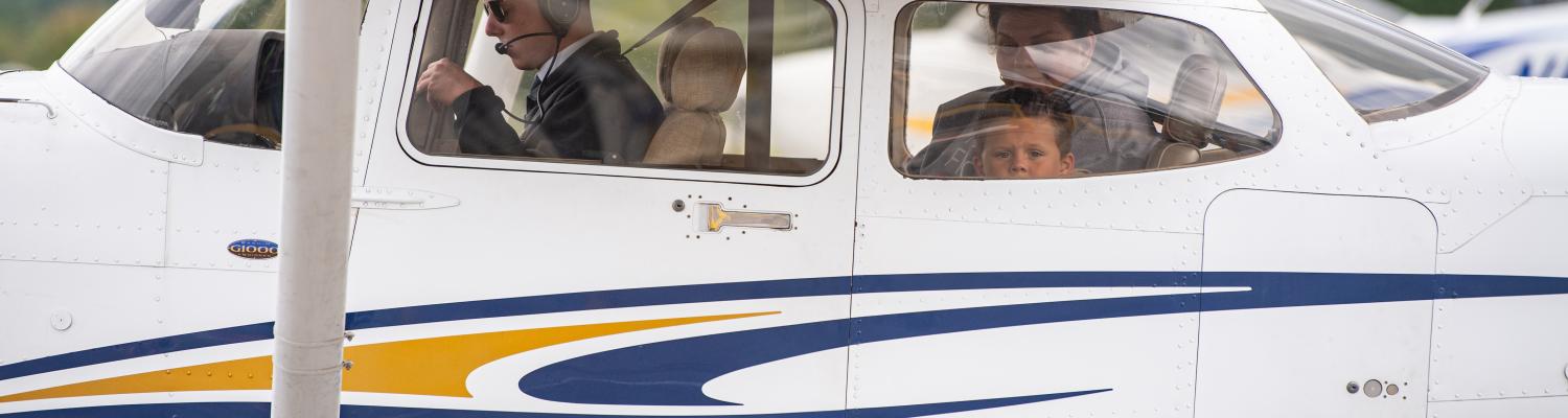 Three children sit in the back of a single-engine airplane as it takes off.