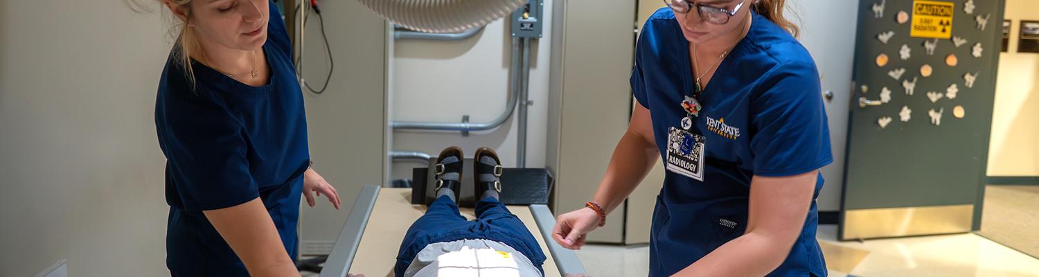A female radiologic technology instructor assists a female student with a piece of x-ray equipment
