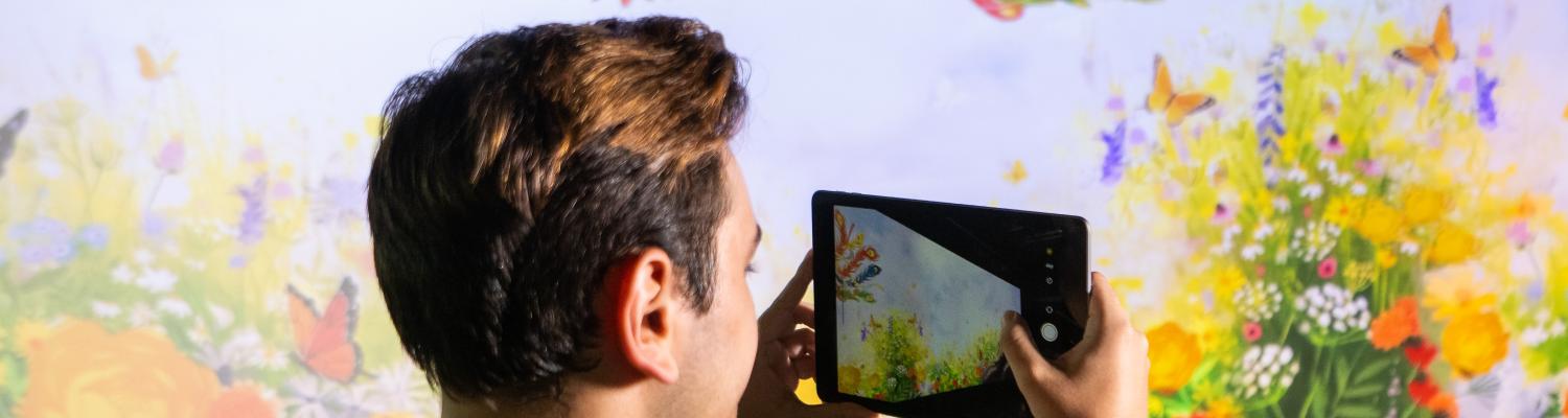 photo of student holding ipad with colorful background projected on a screen