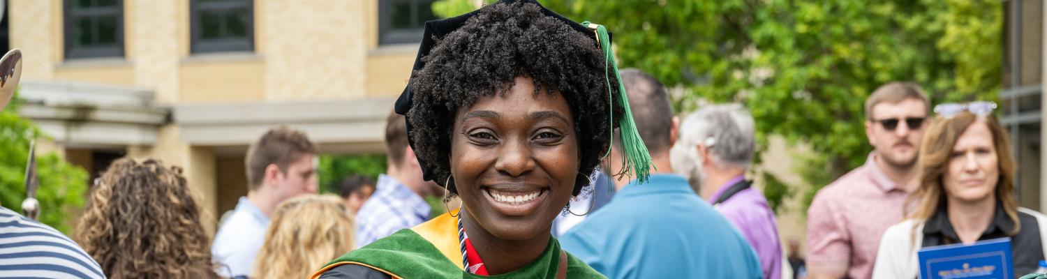 A woman smiles wearing graduation regalia.