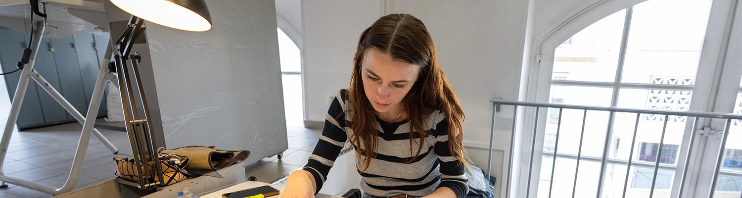 A photo of a young woman working at a desk strewn with papers
