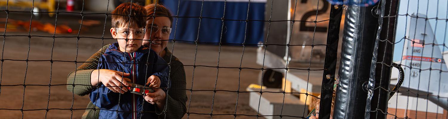 A child flies a small blue drone inside a safety net at the A&E Expo