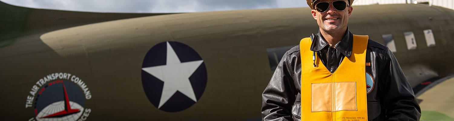 A pilot in period correct World War 2 pilot uniformposes in front of a Douglas C-53 Skytrooper