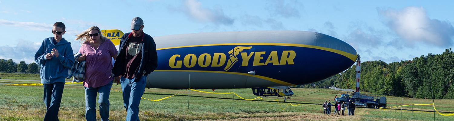 A family walks towards the camera as they leave the area for viewing the Goodyear Blimp.