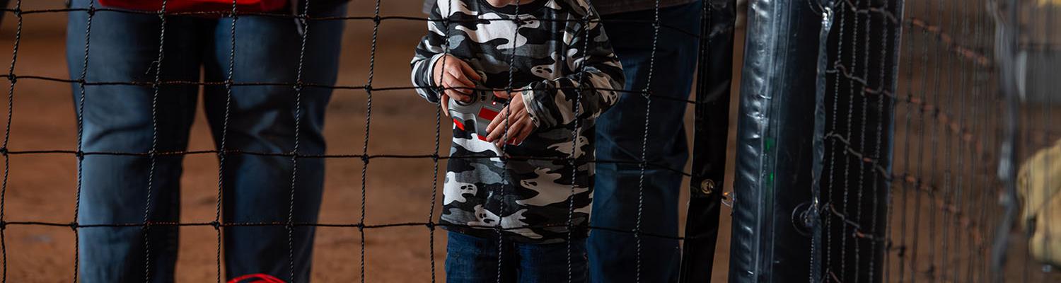 A child flies a small red drone inside a safety net at the A&E Expo