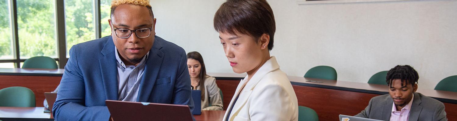 A man and a woman in suits, one holding a laptop while the other watches