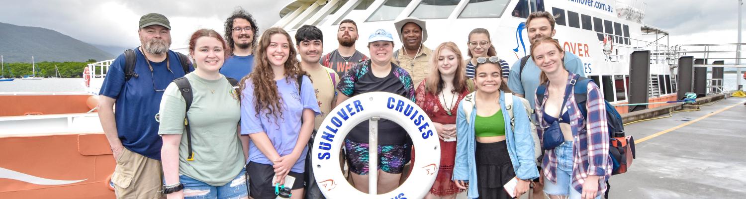 group of students standing in front of a boat