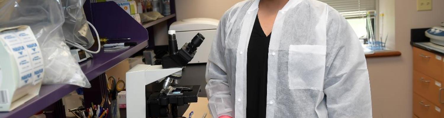 Student in science lab standing next to microscope