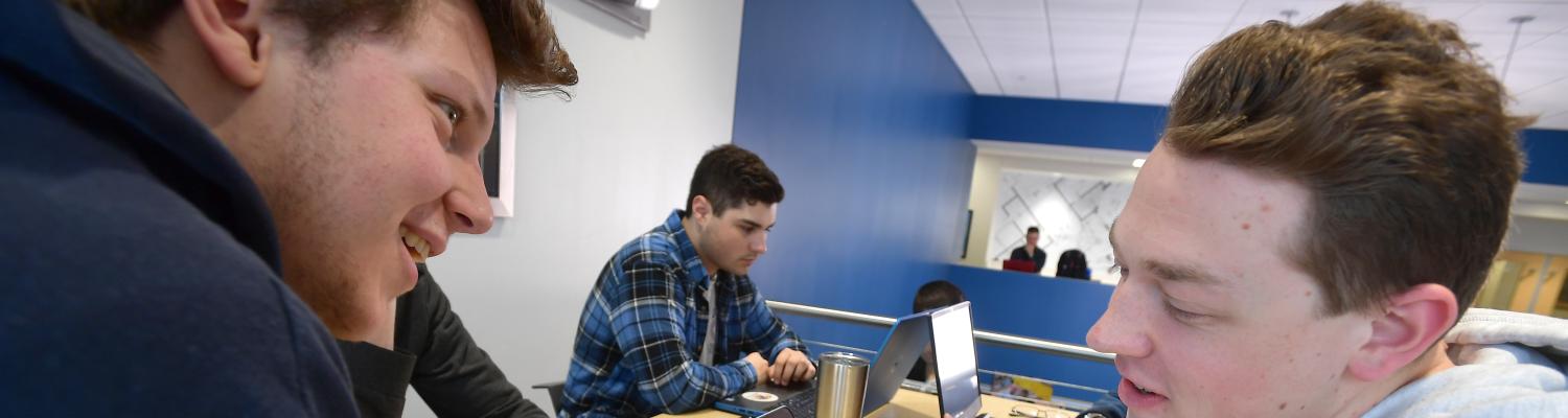 Two students sitting at table in the Peer Tutoring area at the College of Aeronautics and Engineering with a laptop and smartphone for a tutoring session. 