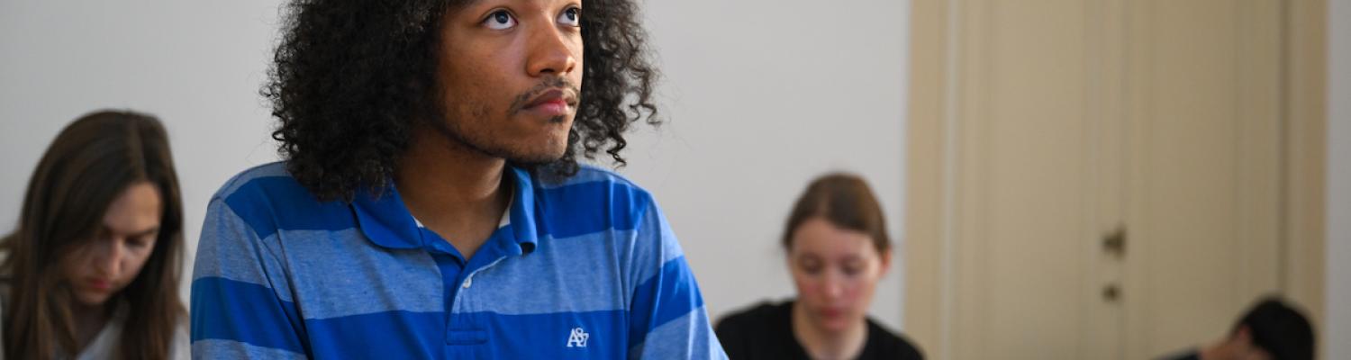 Male student in blue shirt sitting in class taking notes.