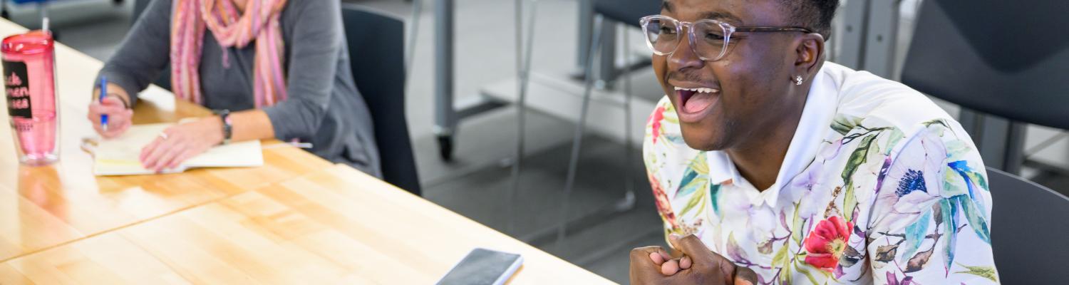 Student sitting at desk with a laptop, showing an excited face.