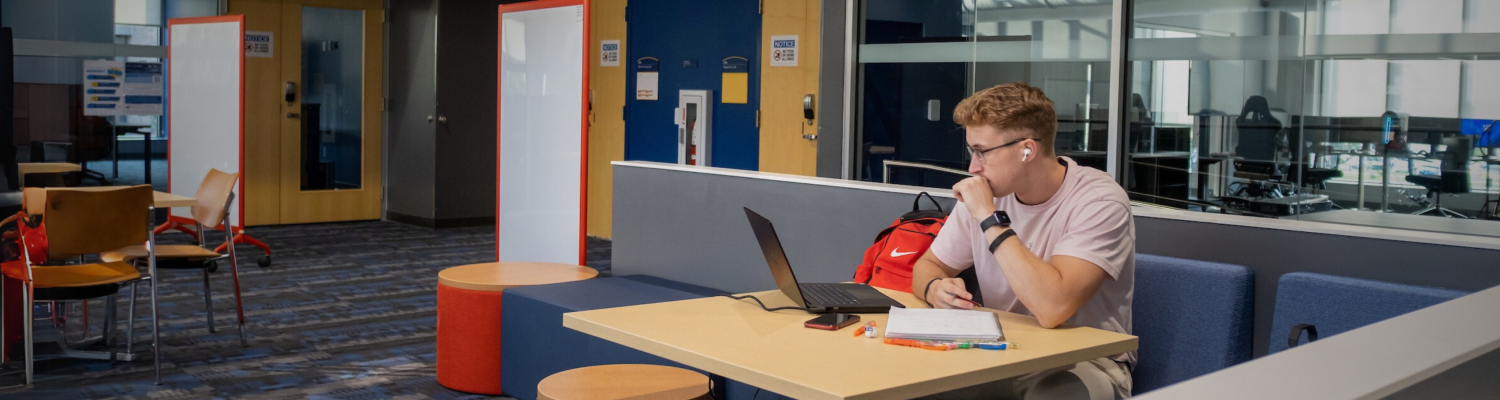Male student in communal room with glass walls and bright blue and red carpet
