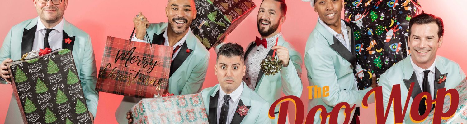 Six musicians from The Doo Wop Project wearing matching light blue suits, each holding a Christmas present and posing together for a festive holiday photo.