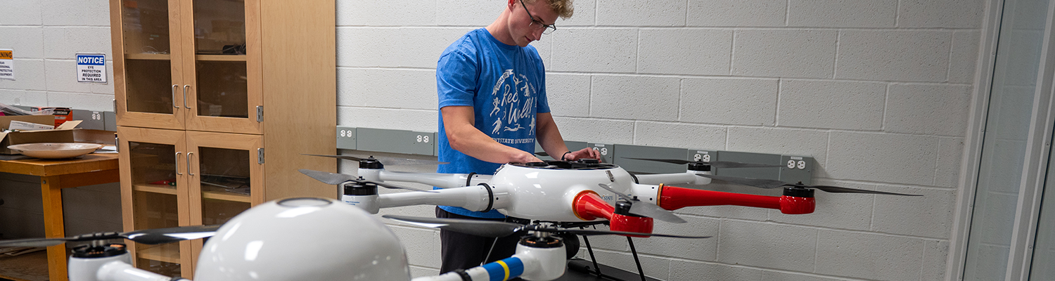 A male student makes adjustments to a medium quadcopter drone in the Drone Lab