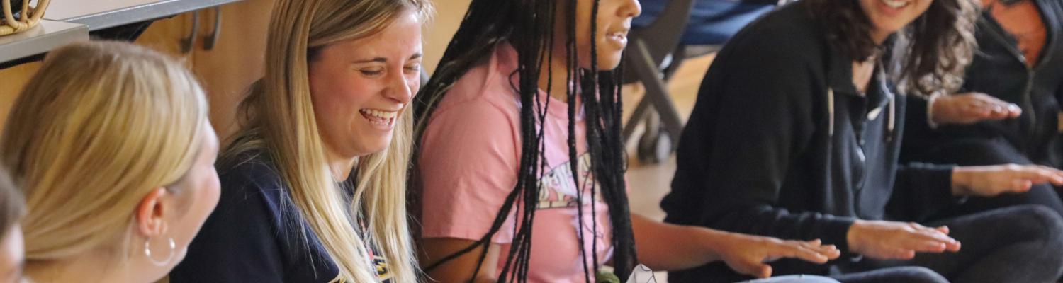 Early Childhood Education students sitting in a circle on the floor laughing during a music demonstration class.