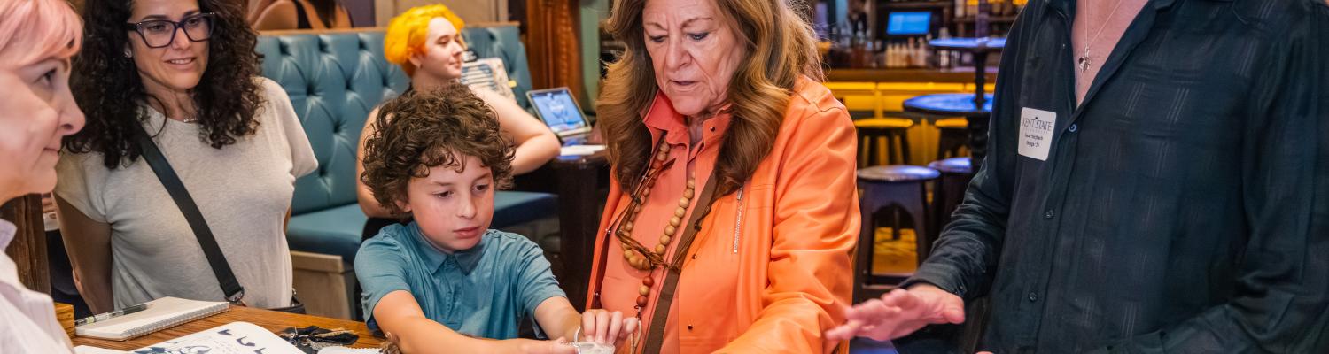 Fern wears an orange shirt and studies technical drawings with other students