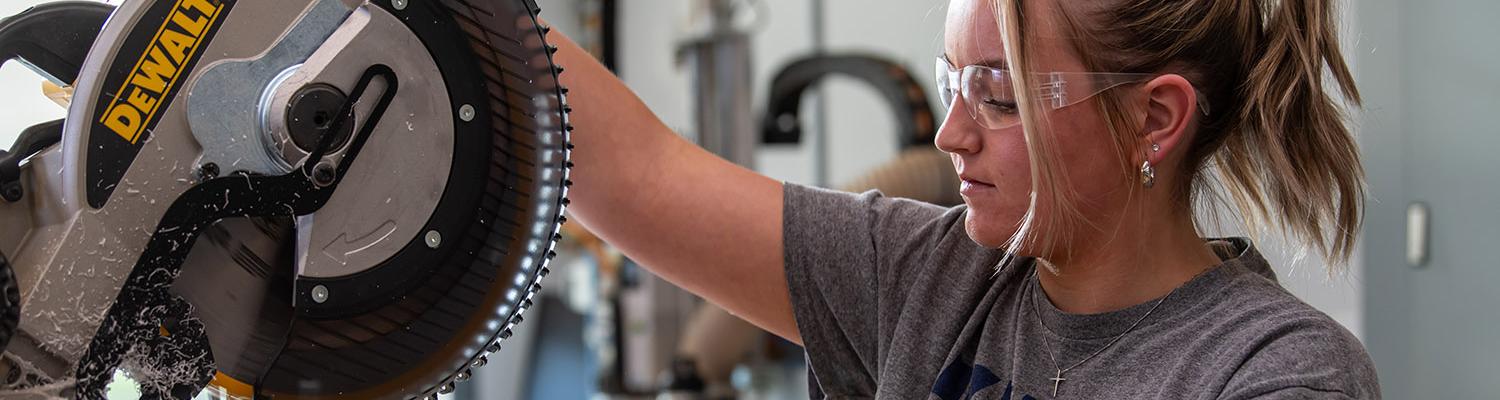 A female student uses a mitre saw in the Pattern and Fabrication Lab