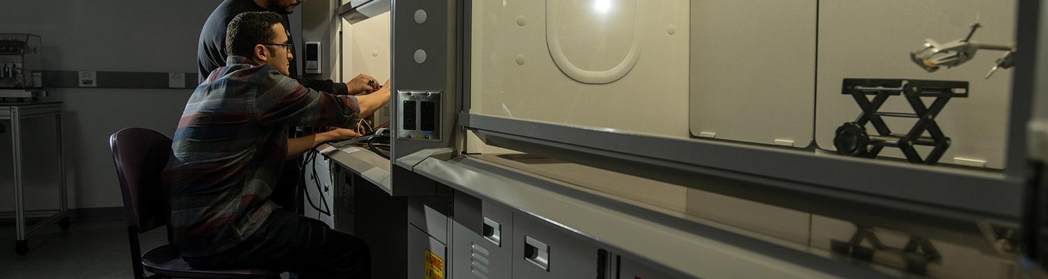 Two male students examine a project under a fume hood in the Flex Lab