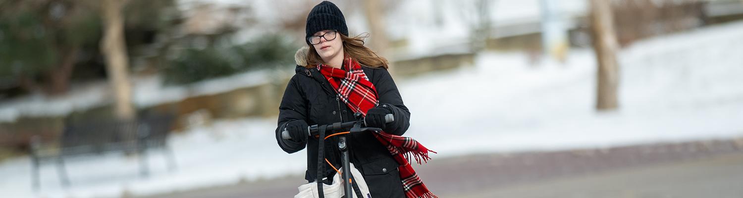 Photo of a student riding an electric scooter across campus in the snow