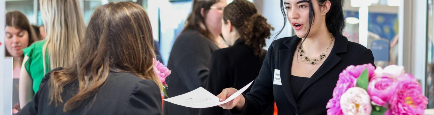 Hospitality and Event Management Career Fair attendee handing her resume to a recruiter.