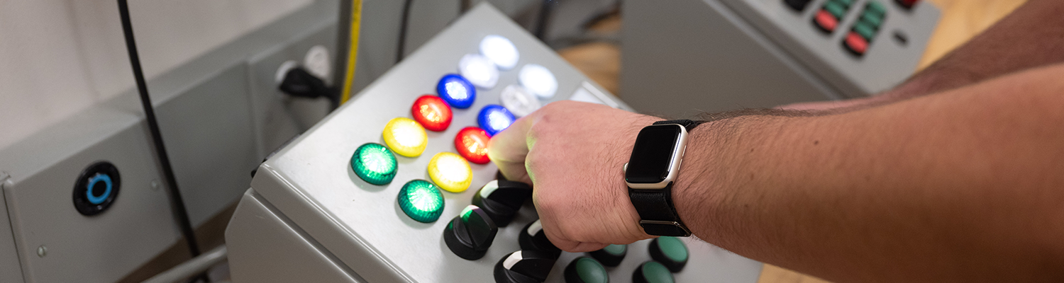 close-up of an an angled control box with multicolored lights being turned on and off by a person's hand