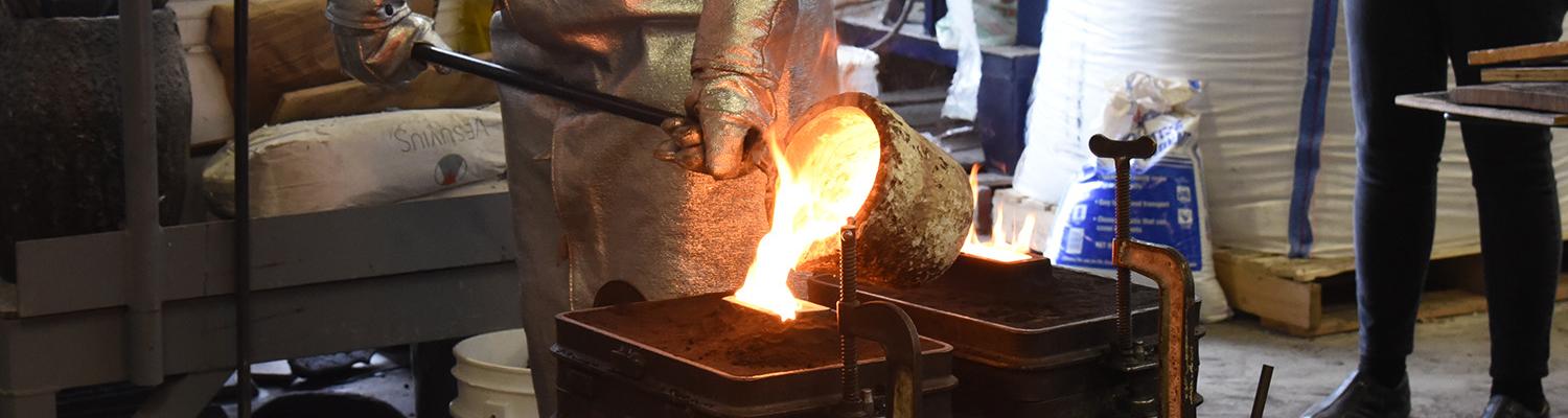 A student pours molten metal from a crucible into a mold