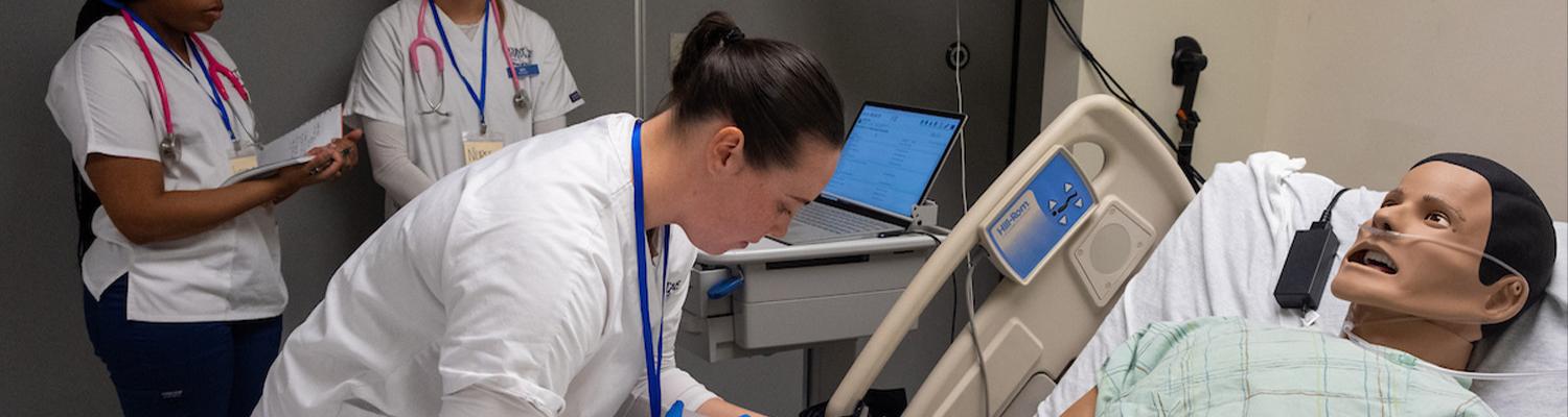 A Kent State University nursing student administers IV medication to a manikin during a simulation while two classmates observe. (Photo credit: Bob Christy)