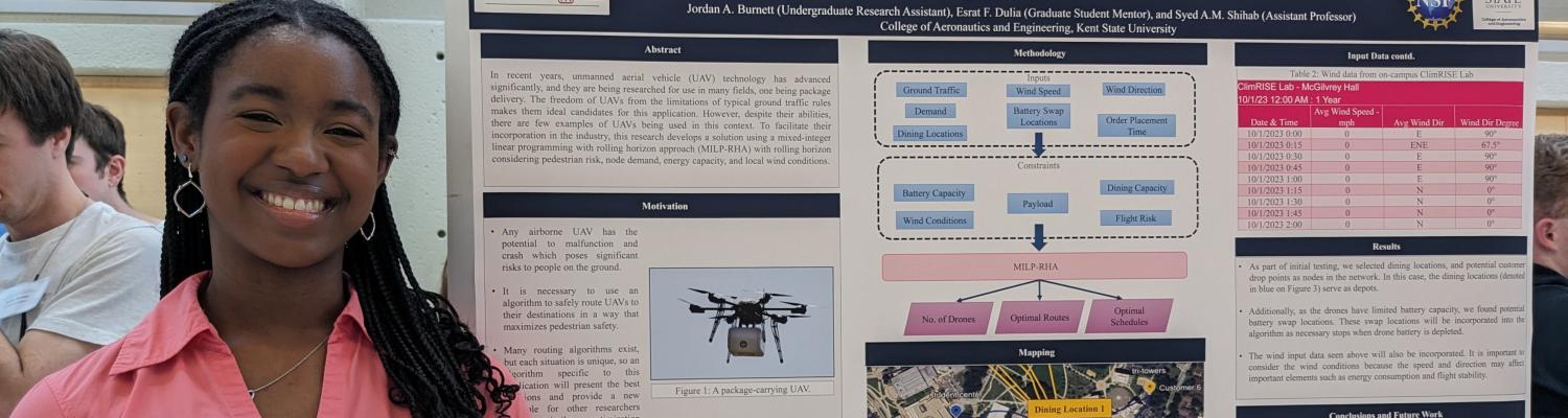 Engineering student Jordan Burnett stands next to a poster describing her project, "Safe Routing and Dispatching of Package Delivery UAVs under Varying Wind and Flight Risk Conditions."