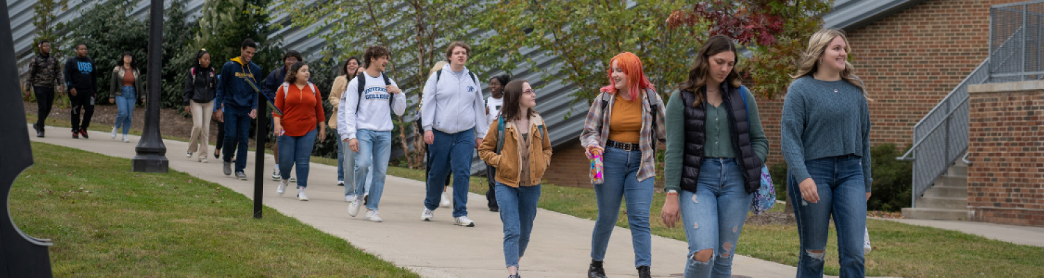 long line of students walking in pairs down a 51���� Sidewalk with brick building in the background