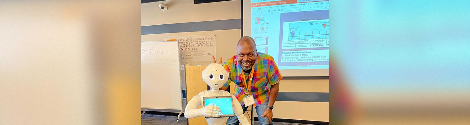 Alumnus Trevor Watkins poses with a robot holding an iPad