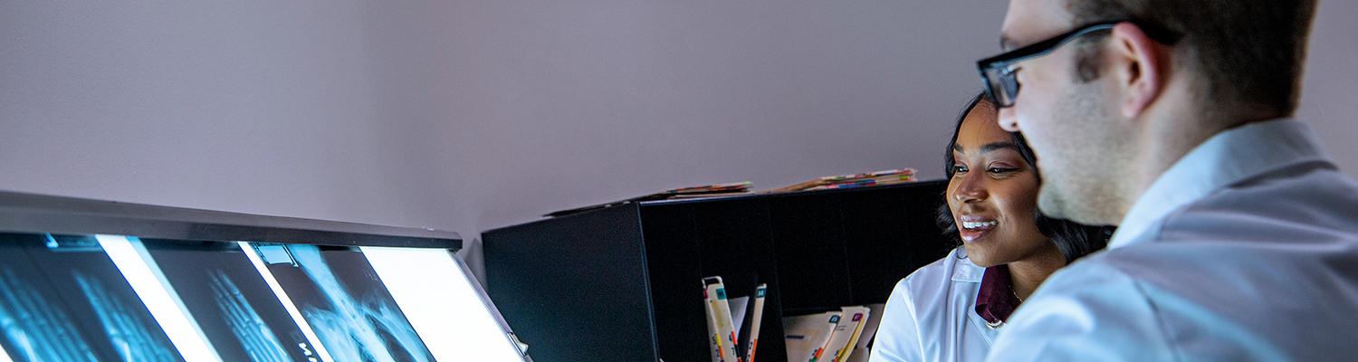 A photo of a man and a younger woman in lab coats looking at x-rays.