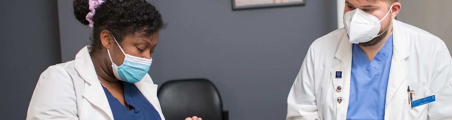 Two podiatry students with masks on inspecting a patient's foot.