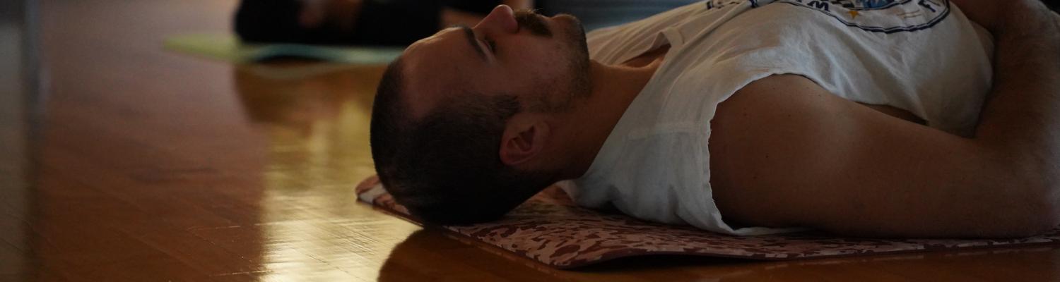 Two individuals lying on their backs with their eyes closed during a yoga session with their hands resting on their stomachs 
