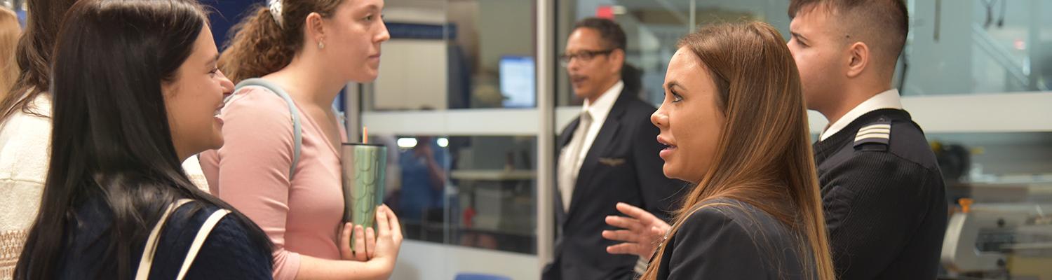 Two female students speak with a female and a male pilot at the College of Aeronautics Career Fair