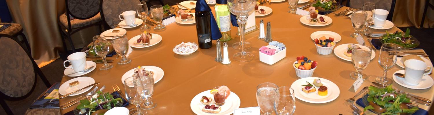 A round table set-up with plates with food and glasses for a catered event