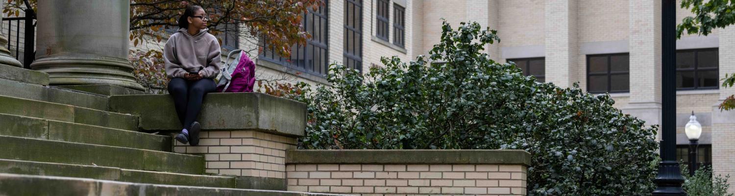 A photo of a student sitting on the stairs outside of a lecture hall
